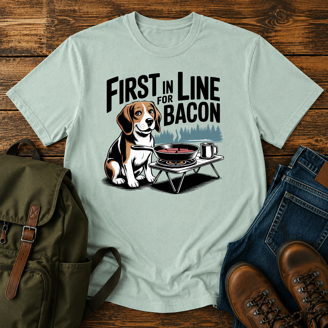 Beagle beside cast-iron skillet on camp stove with tin mug and enamel plate on t-shirt